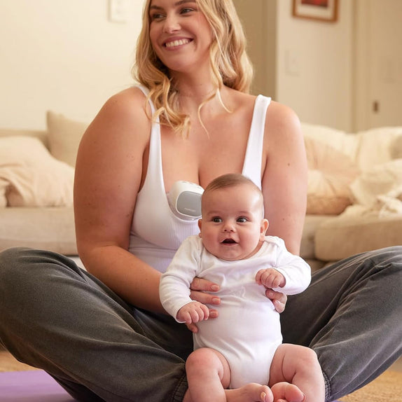 Woman sitting on a yoga mat with a baby on her lap, wearing momcozy S9 breast pump