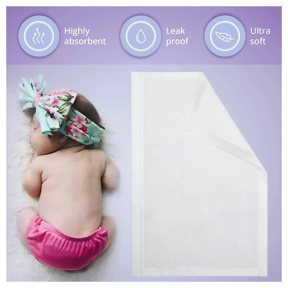 A baby wearing a pink diaper and a floral headband lies on a white blanket next to a white absorbent diaper pad, with three feature icons at the top reading Highly absorbent, Leak proof, and Ultra soft.